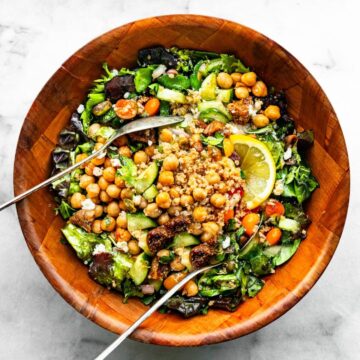 brown bowl of Moroccan salad with quinoa with serving utensils nestled in the salad