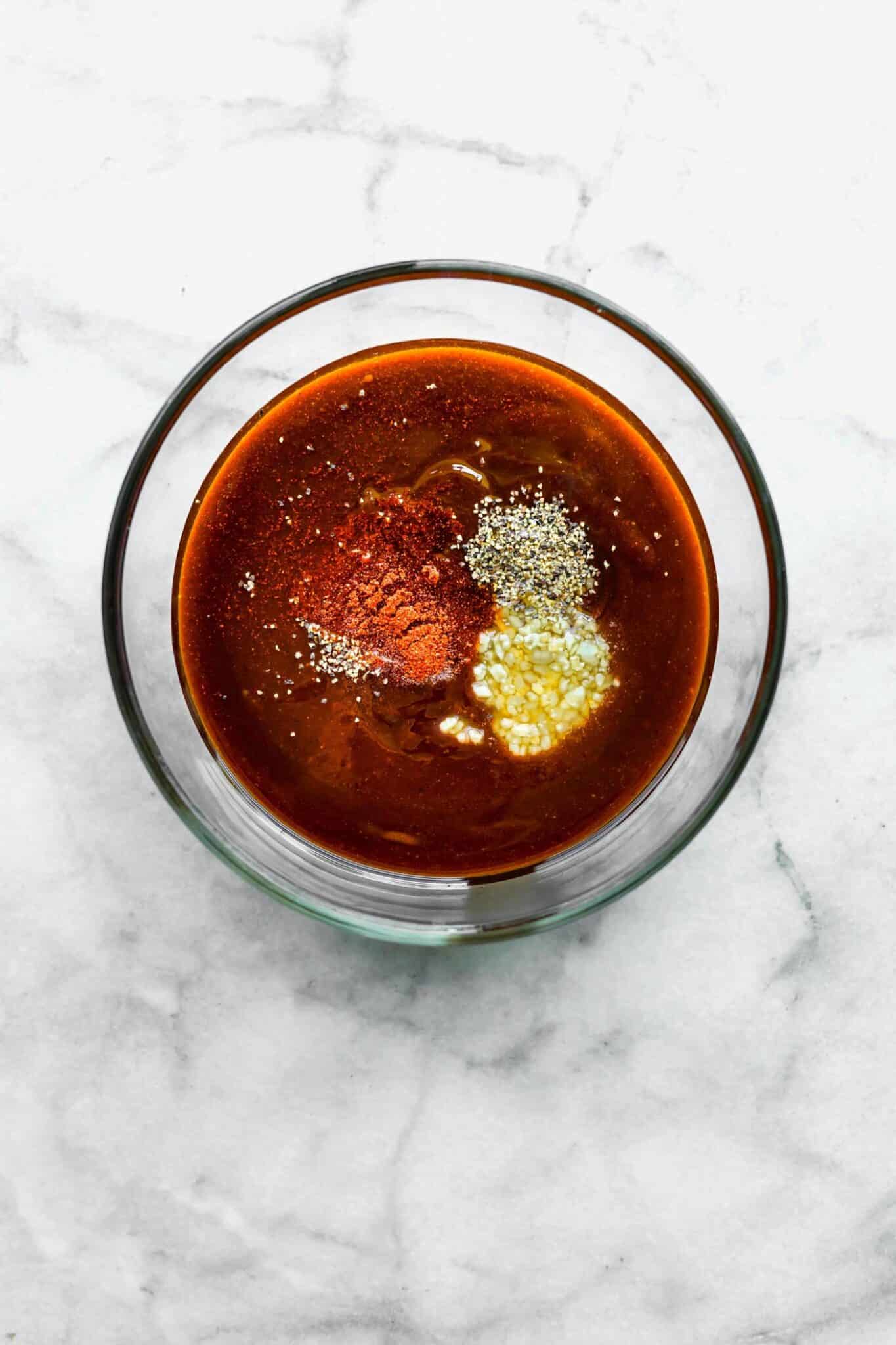 BBQ sauce ingredients in a glass bowl on a white marble countertop.