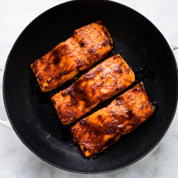 Overhead photo of three baked barbeque salmon filets in a cast iron skillet.