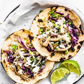 2 pork tacos with red cabbage and cilantro on top. Lime on side. Sitting on a white plate