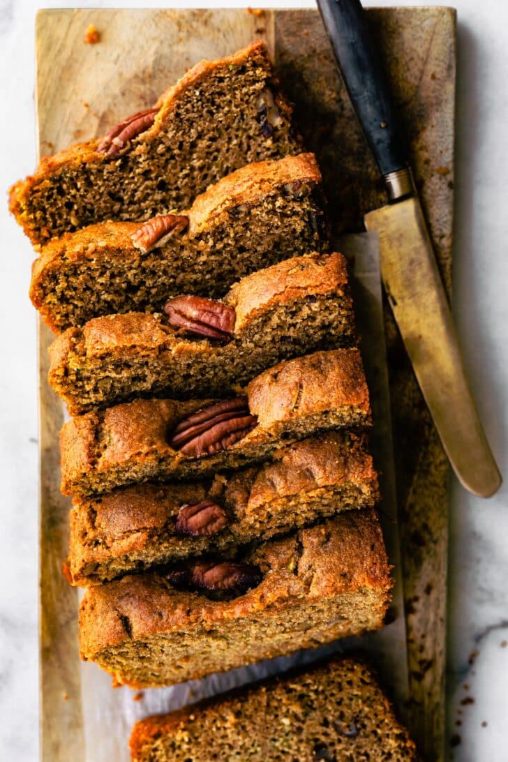 overhead photo of sliced zucchini bread with walnuts on top and knife laying next to it