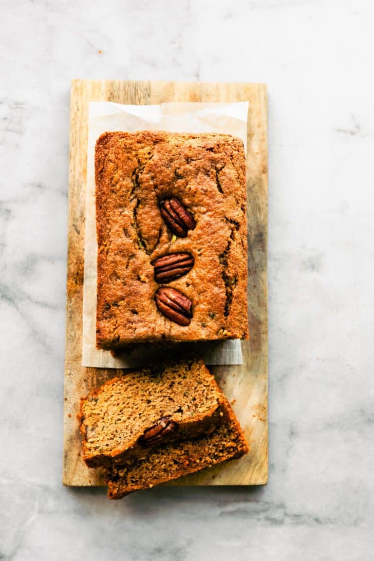 overhead photo of partially sliced zucchini bread with walnuts on top on a wood plank