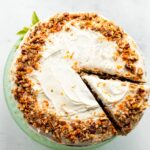 A slice of carrot cake cut out of a round cake on a cake stand.