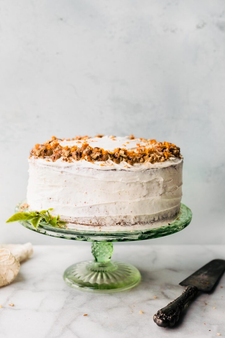 A two tiered round cake with white cream cheese frosting on a green cake stand.