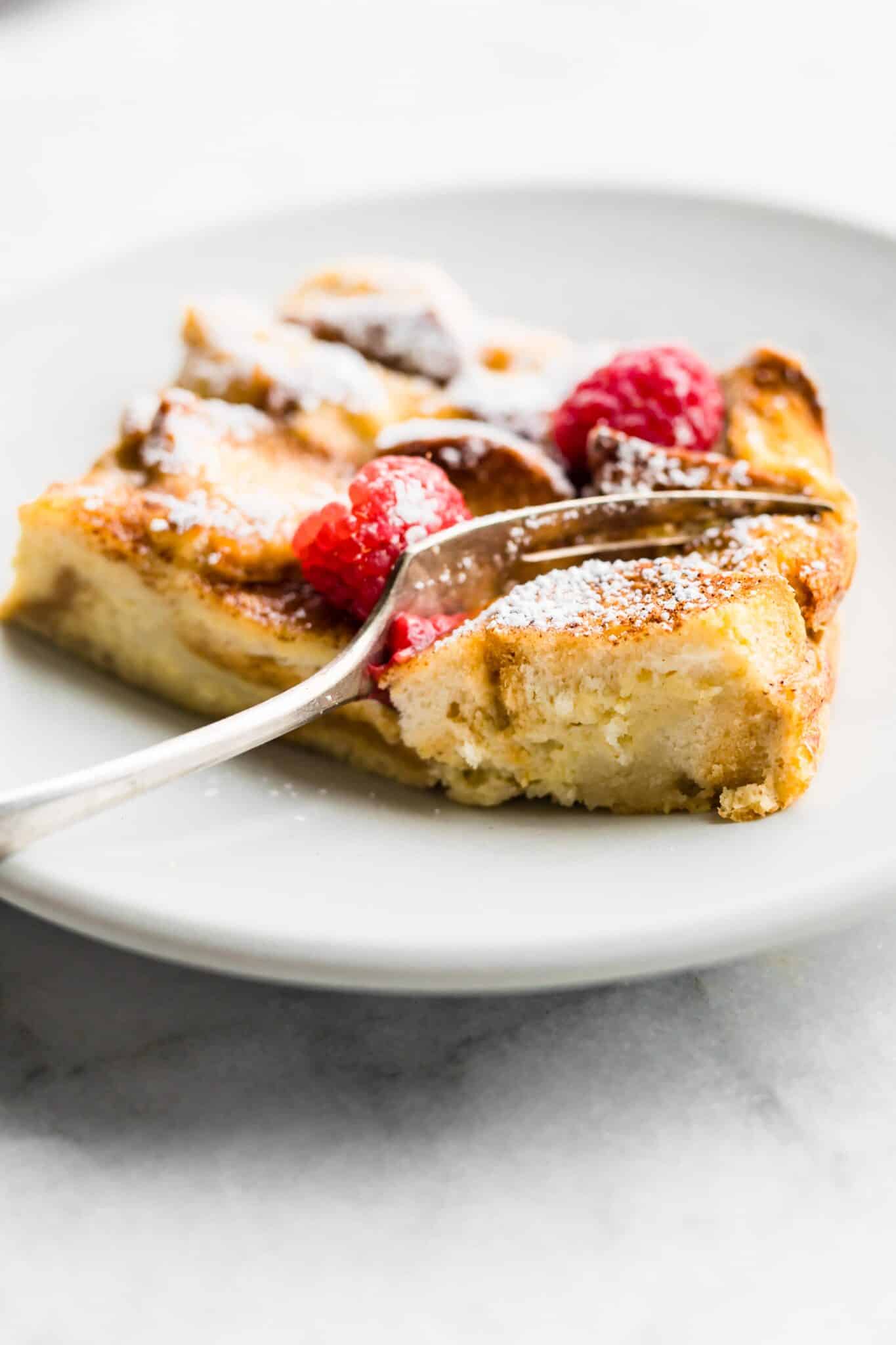 A fork slicing into a slice of gluten free French toast casserole on a white plate.