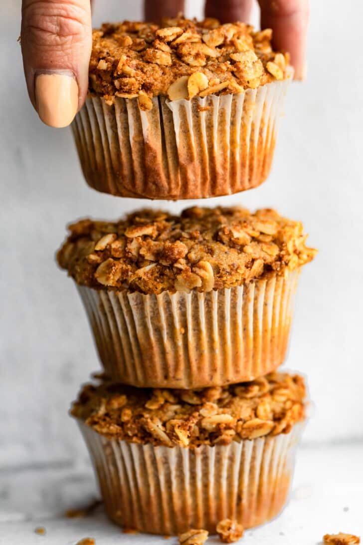A stack of three muffins with a woman's hands lifting the top muffin off.