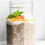a jar of chia pudding with protein with layers of dairy-free yogurt, honey, peaches, and fresh mint on top