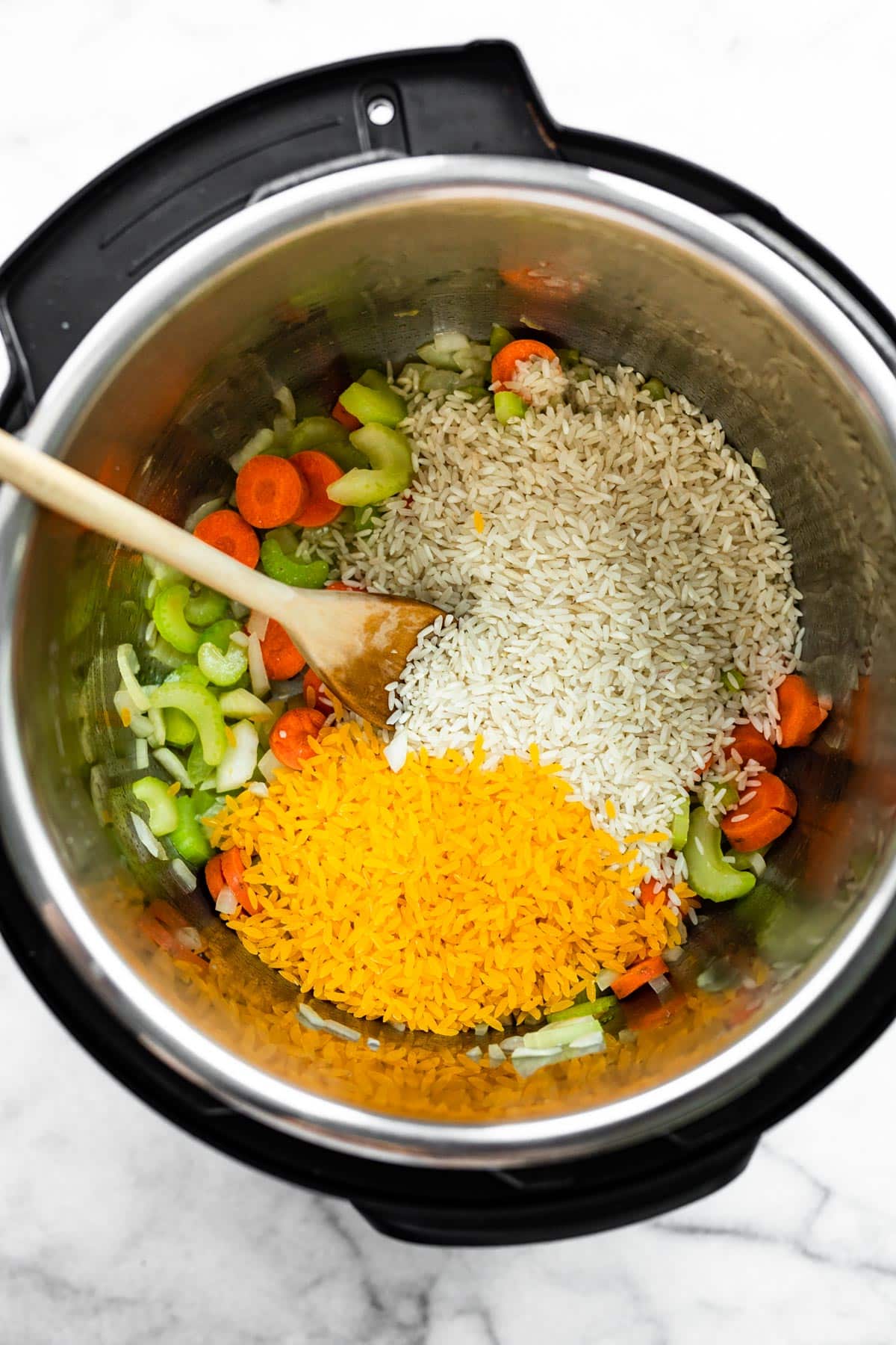 long grain rice, celery, carrots, and gluten free orzo in an instant pot with a wooden spoon sticking out