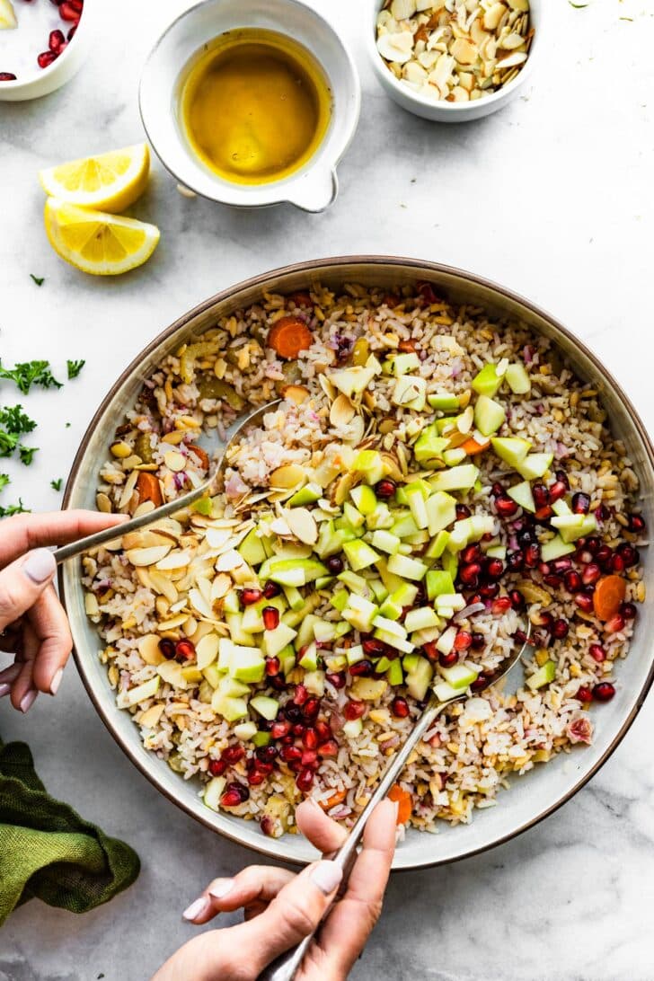 two hands mixing ingredients for rice pilaf with orzo