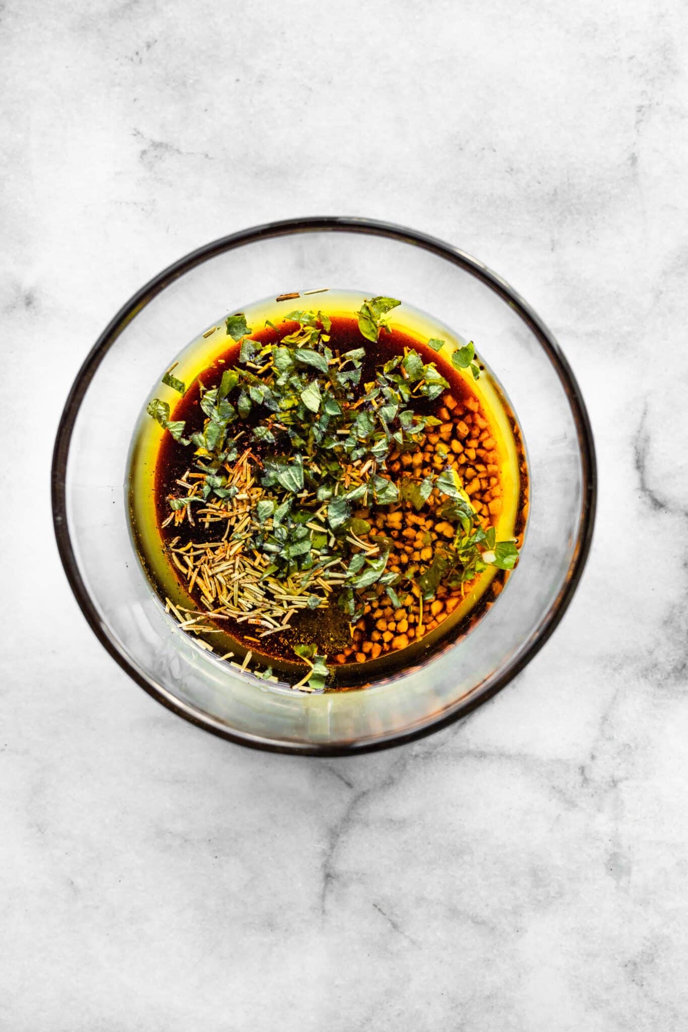 A glass bowl with oil, seasonings and vinegar.
