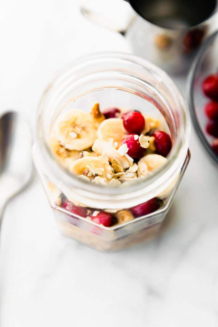 pumpkin overnight oats topped with banana slices and cranberries in mason jar