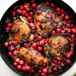 a skillet full of four balsamic roasted cranberry chicken thighs surrounded by roasted cranberries