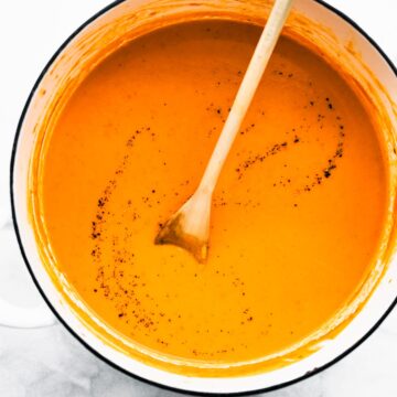 Roasted Red Pepper Soup in a bowl being stirred with a wooden spoon.