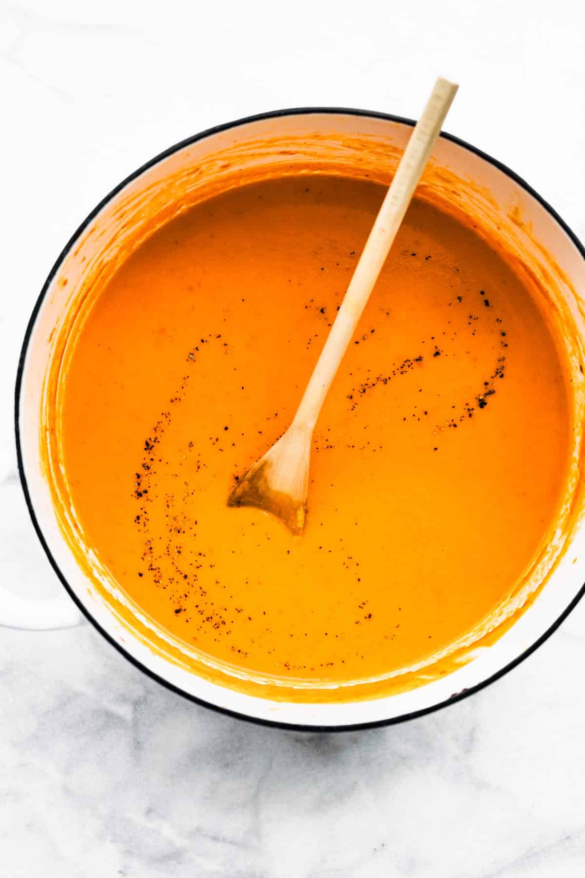 Roasted Red Pepper Soup in a bowl being stirred with a wooden spoon.