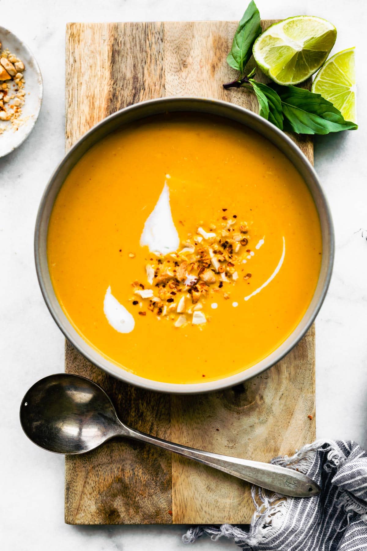 Overhead photo of Thai curried carrot ginger soup on a wooden board with a spoon.