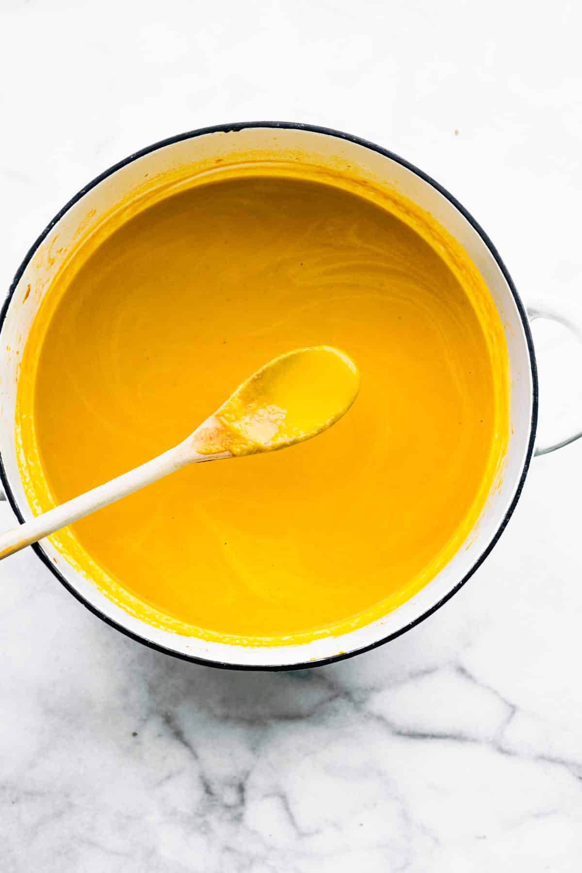 Overhead photo of carrot ginger soup in a white pot with a wooden spoon.