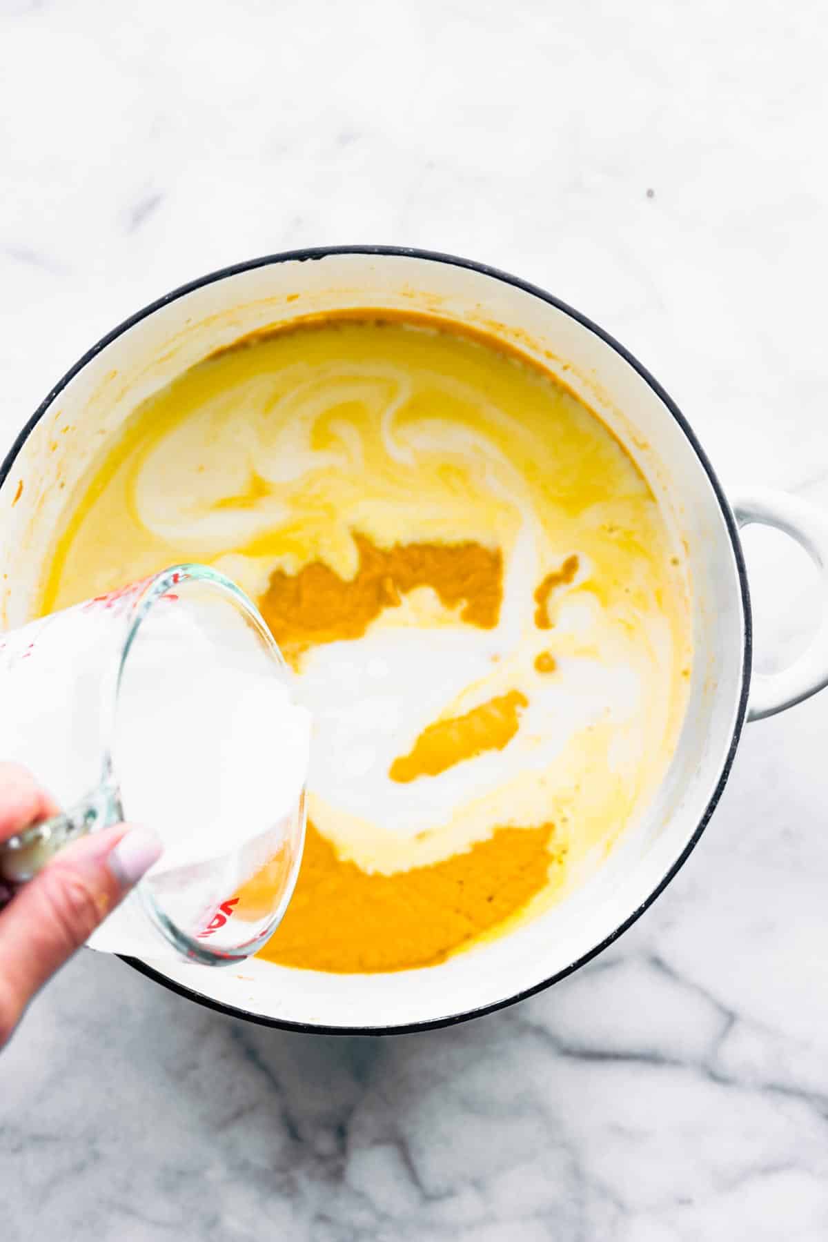 Coconut milk being poured into a pot of thai curried carrot ginger soup.