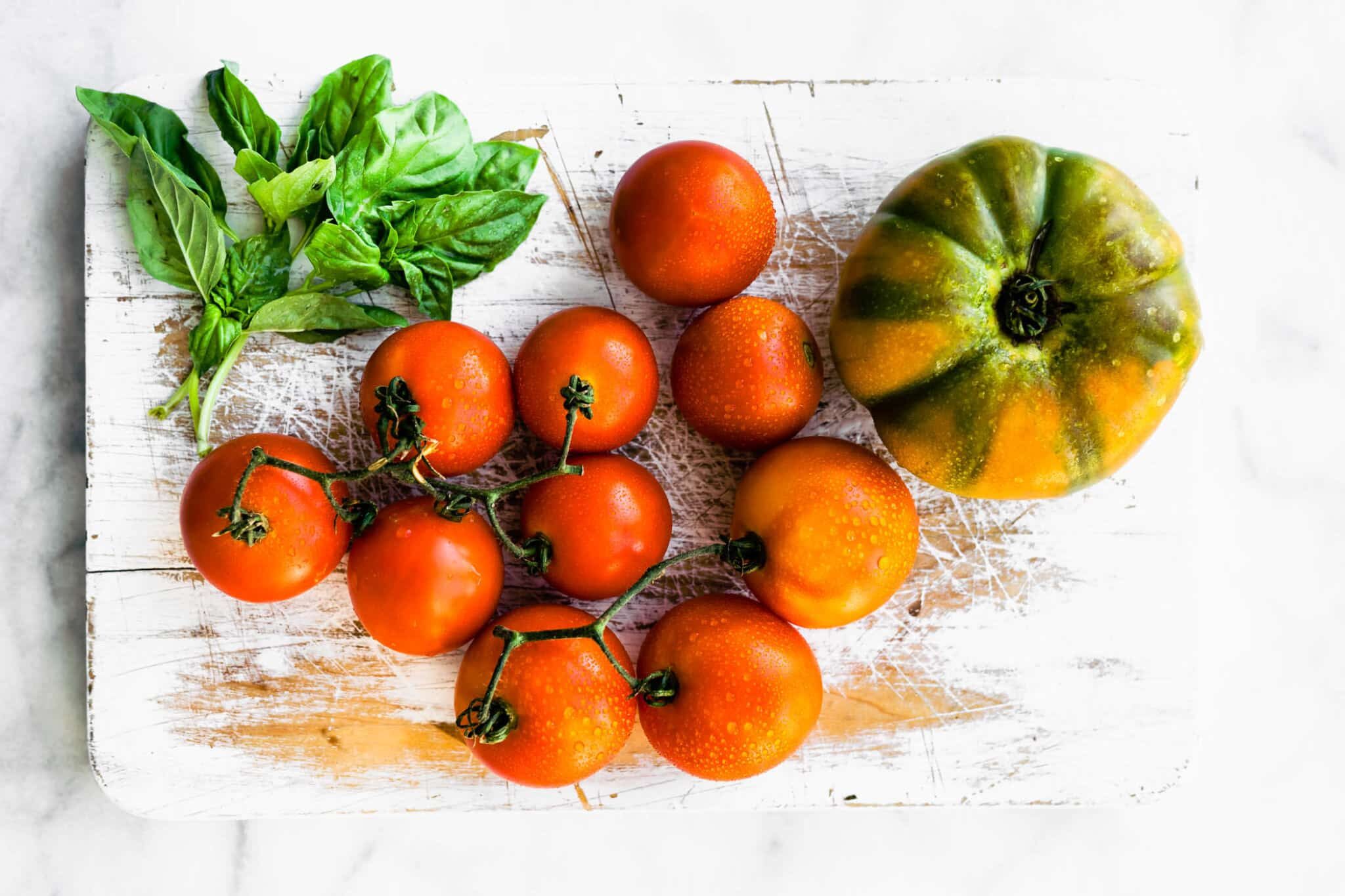 a cutting board with fresh herbs, on-the-vine tomatoes, and a large tomato
