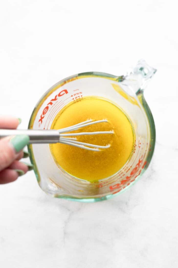Woman's hand whisking salad dressing in a measuring up
