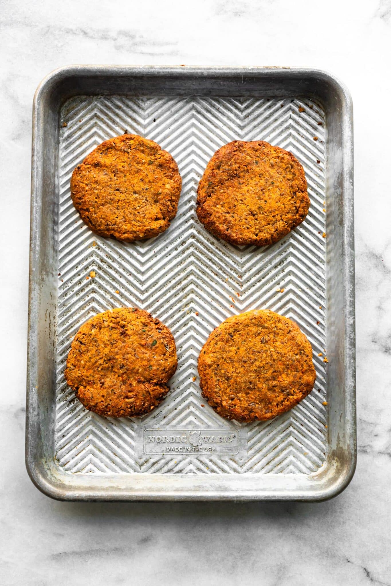 Four golden brown baked veggie burgers on a metal sheet pan.