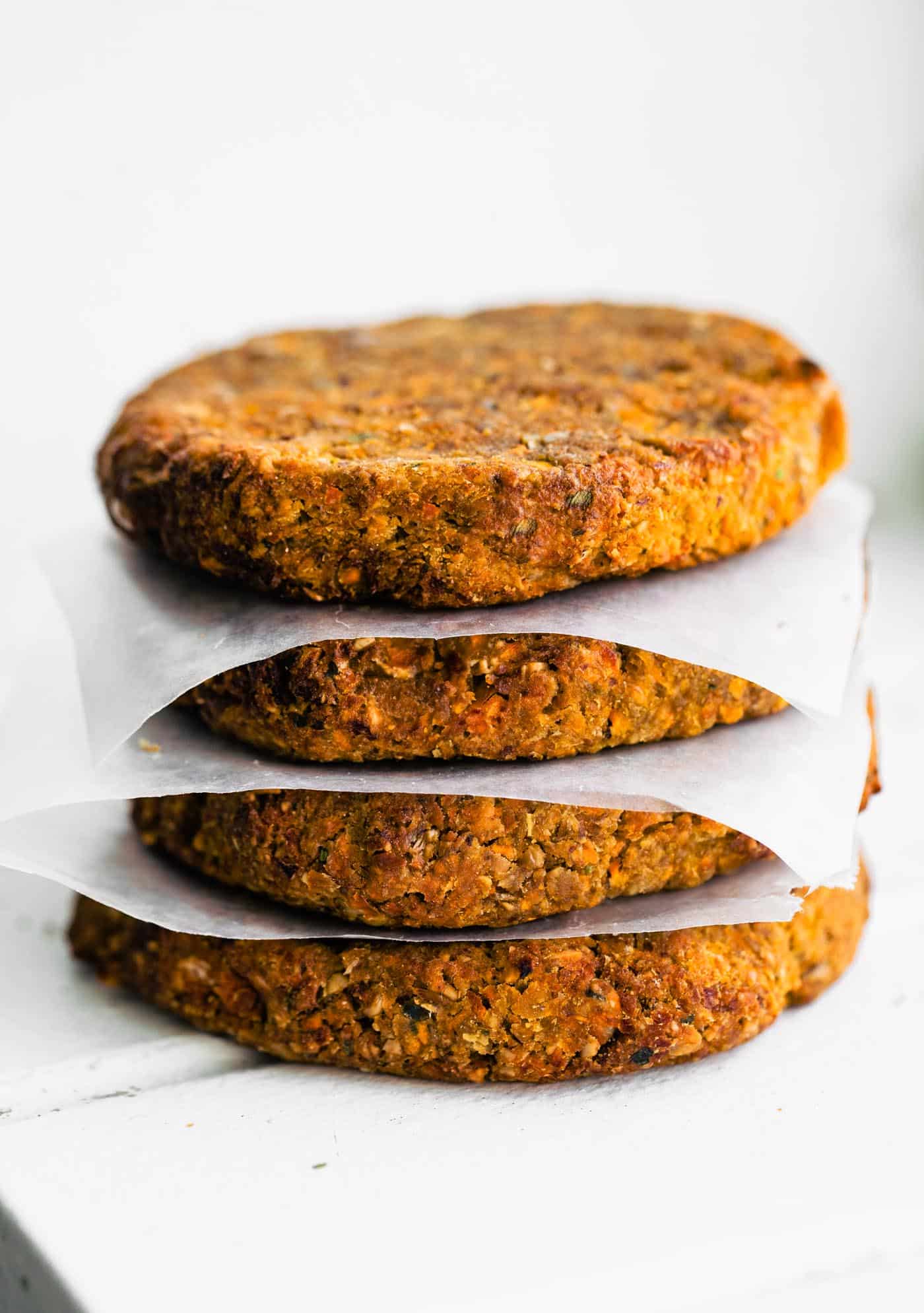 Four baked veggie burgers stacked high with parchment paper between the patties.