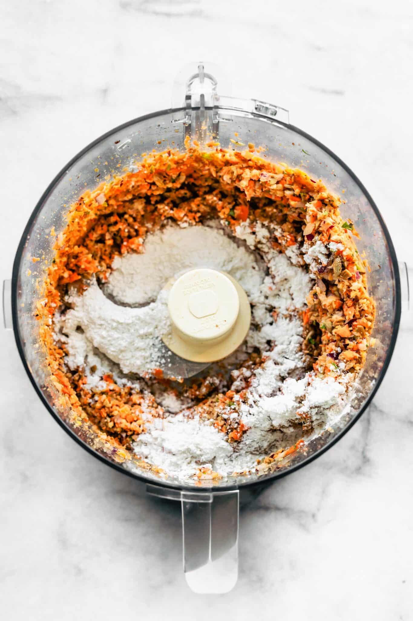 Gluten free flour on top of blended chickpeas and carrots in a food processor.