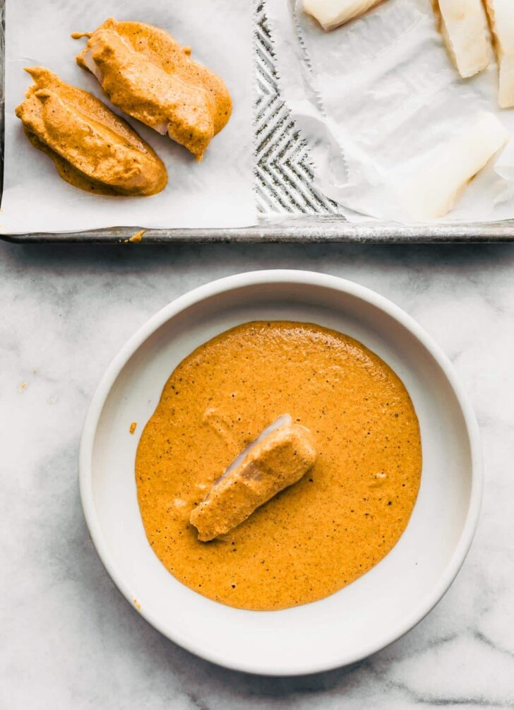 Pieces of raw fish being dipped in gluten-free beer batter.