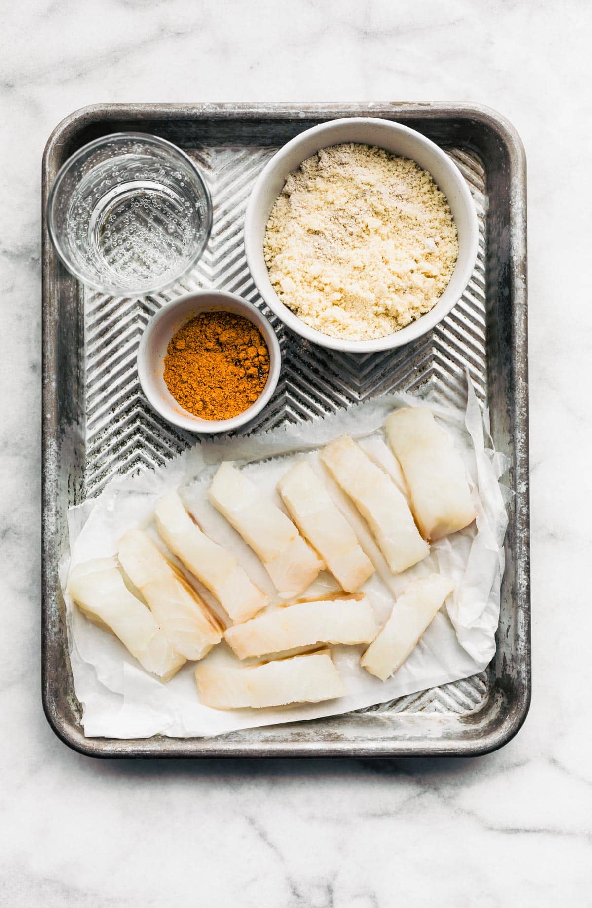 Overhead image of fish pieces, seltzer, and breading.