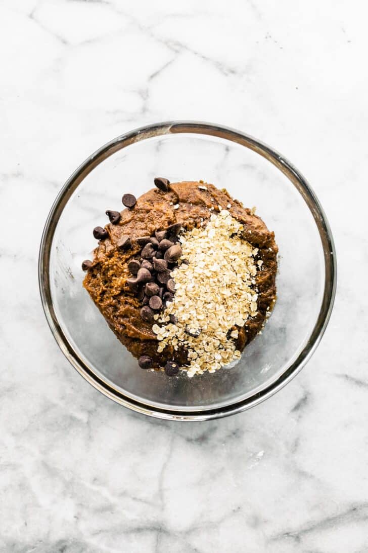 Oatmeal and chocolate chips on top of banana breakfast cookie batter in a bowl.
