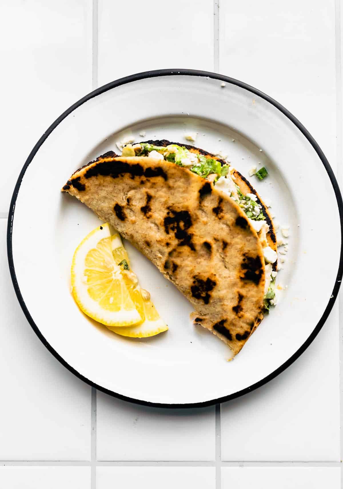 An almost flour tortilla stuffed with chicken and fillings on a plate with two lemon wedges.