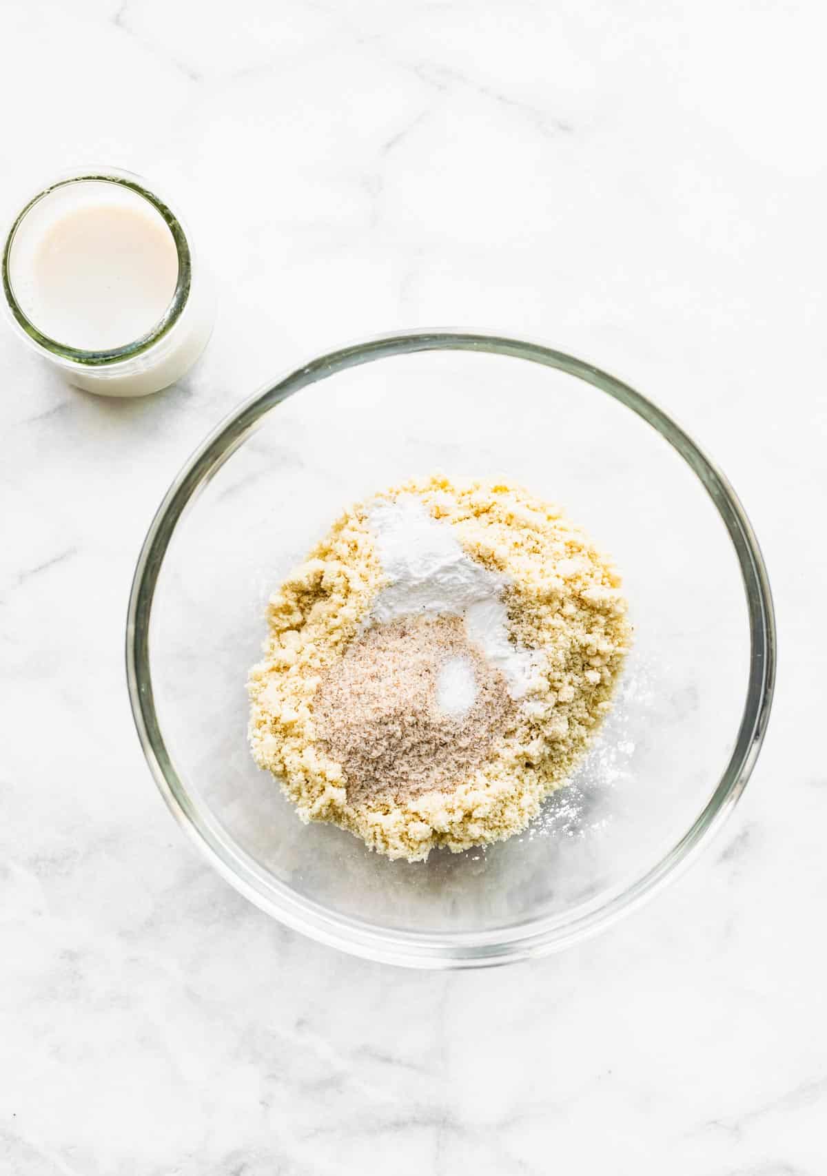 A bowl of dry ingredients and a glass cup of dairy-free milk for almond flour tortillas.