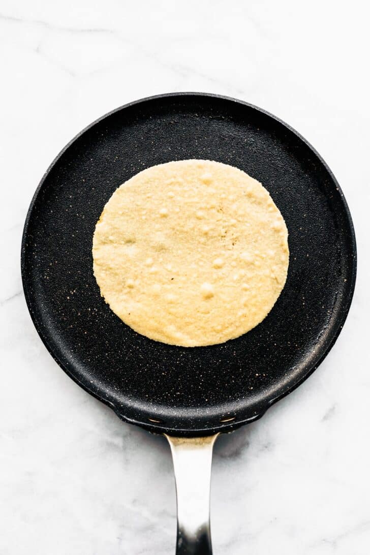 An almond flour tortilla cooking in a skillet.
