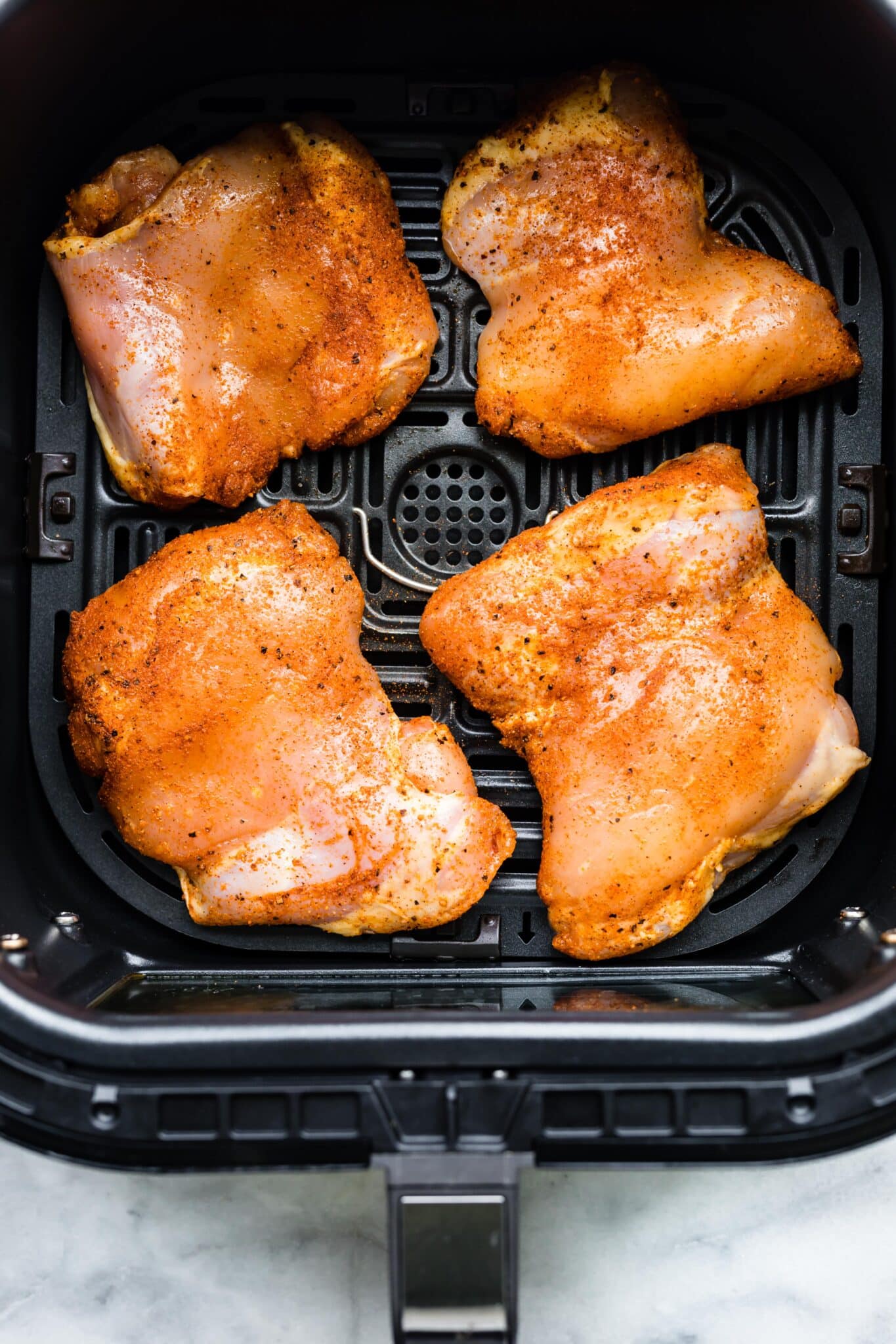 Photo of raw boneless chicken thighs coated in a spice rub in an air fryer.
