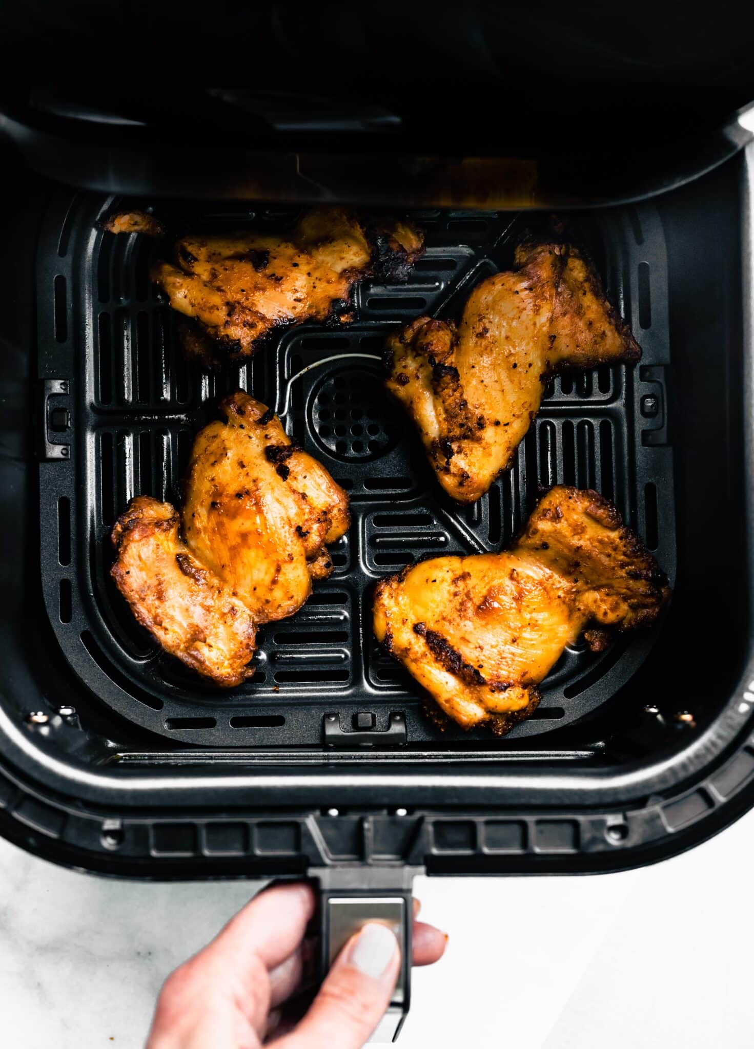 Overhead photo of air fried chicken thighs in a black air fryer basket.