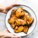 A woman's hands holding a plate of air fried chicken thighs.