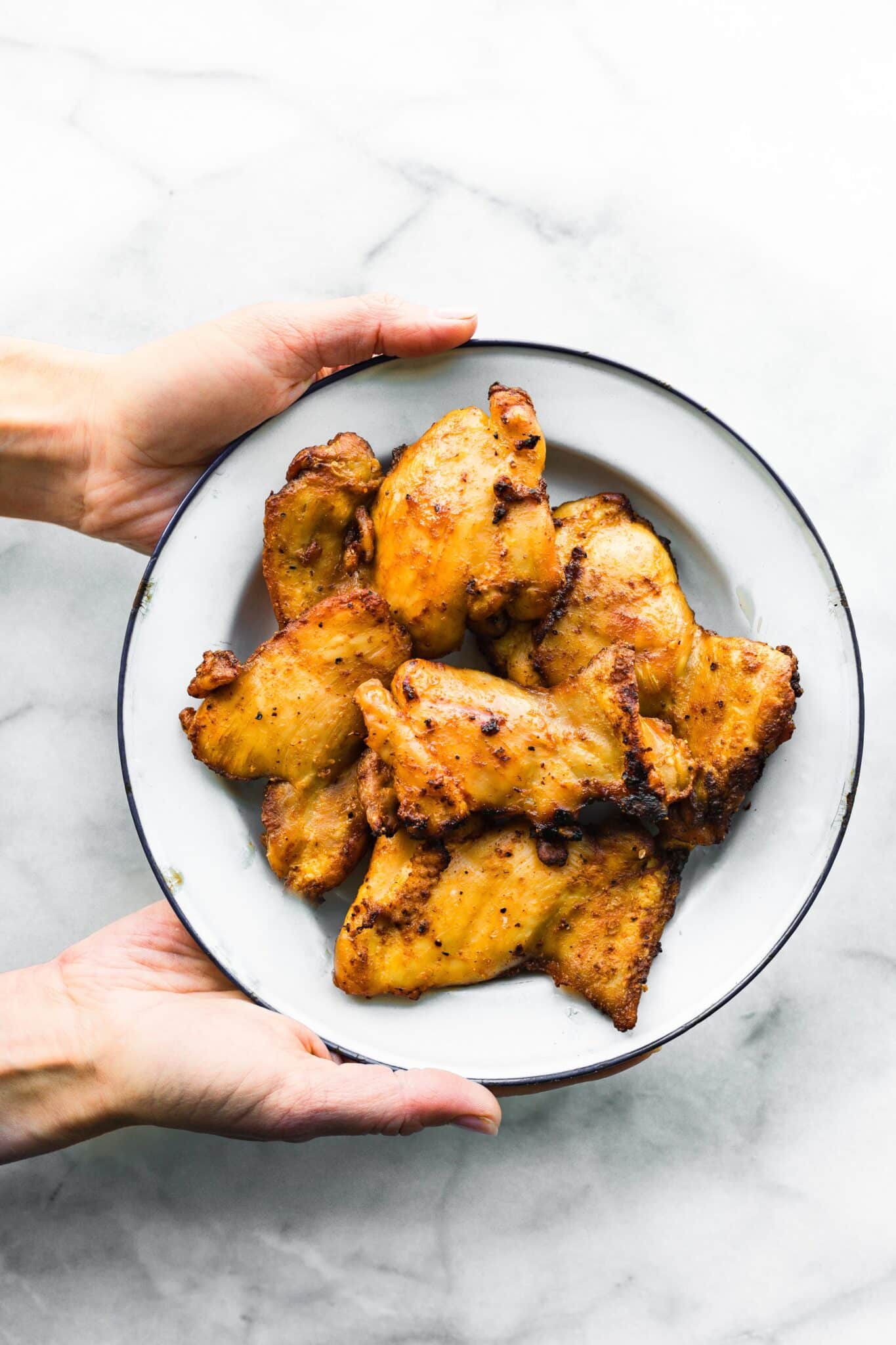 A woman's hands holding a plate of air fried chicken thighs.
