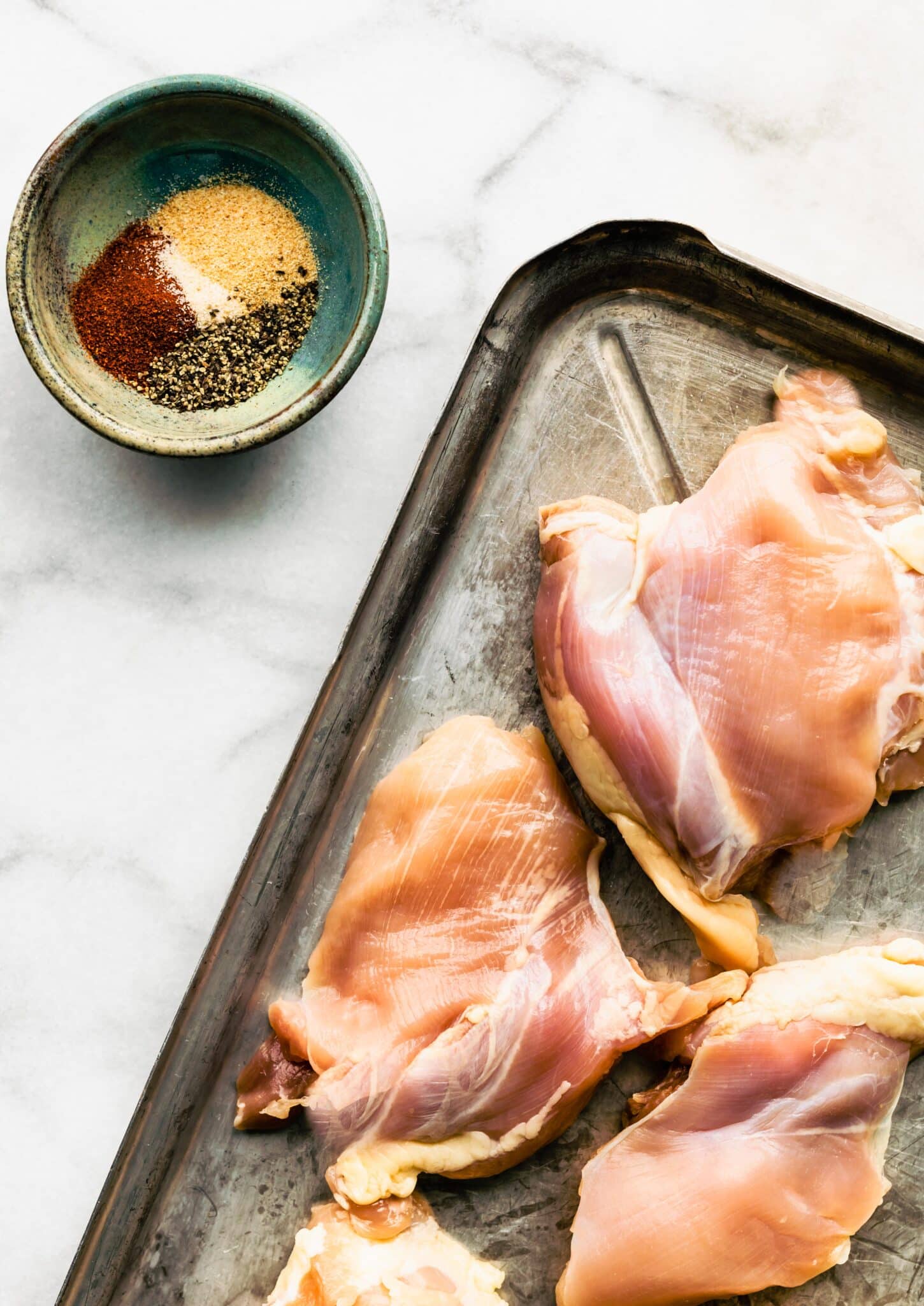 Overhead photo of raw chicken thighs and a bowl of spice mix.
