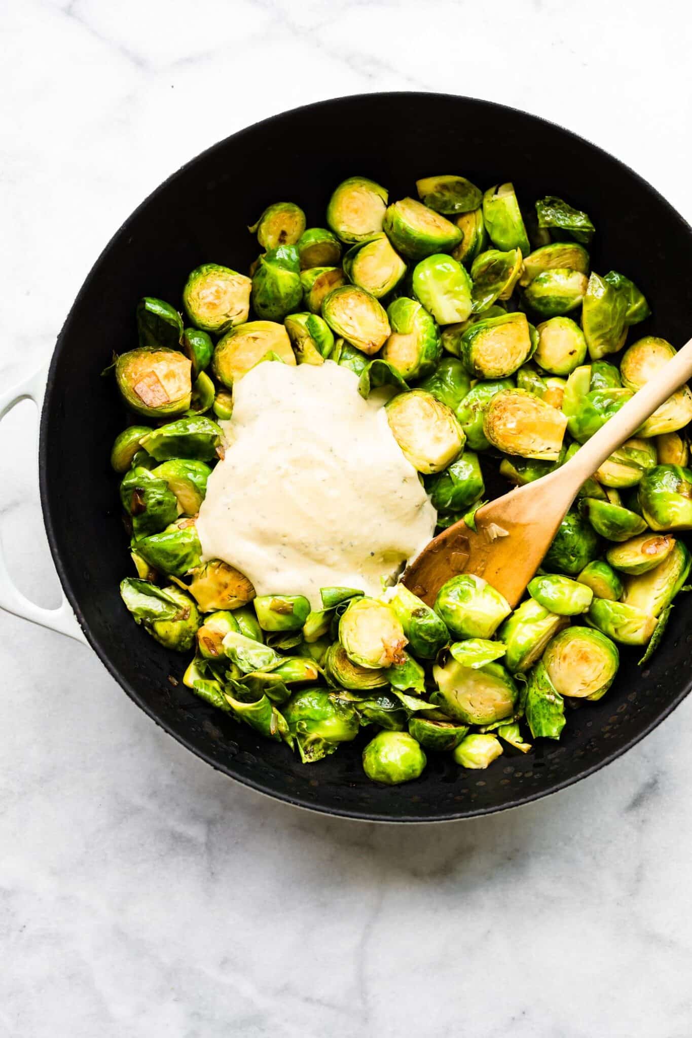 Roasted brussel sprouts in a cast iron pan with a dollop of dressing on top.