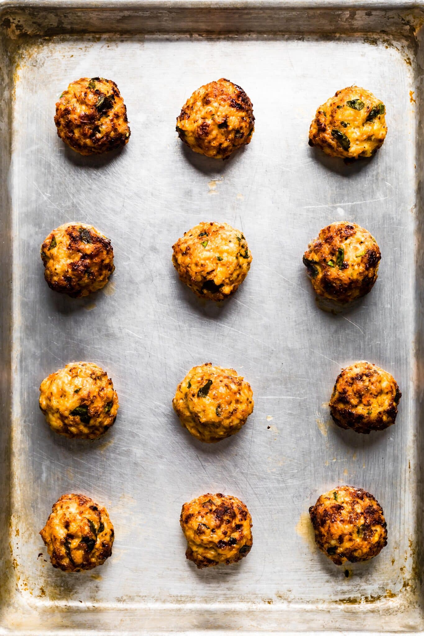 Overhead photo of twelve cooked gluten free chicken meatballs on a sheet pan.