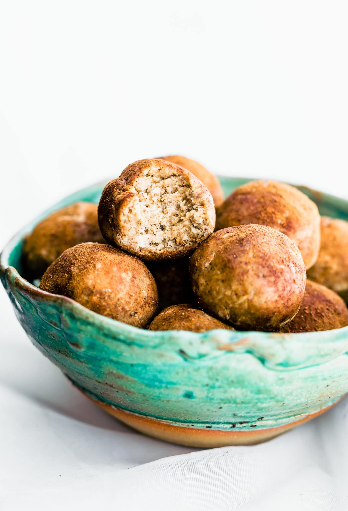 Turquoise bowl filled with cinnamon vanilla protein bites with a bite out of one ball.