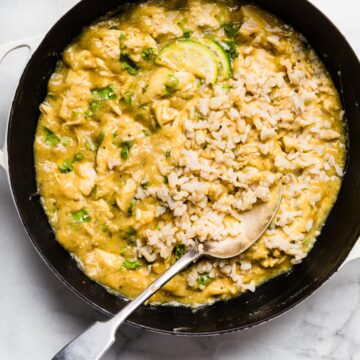 Coconut milk chicken in a cast iron pan with a spoon and rice.