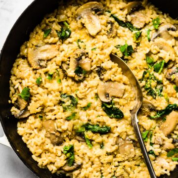 Creamy mushroom risotto in a cast iron pan with spinach and cheese with a spoon.