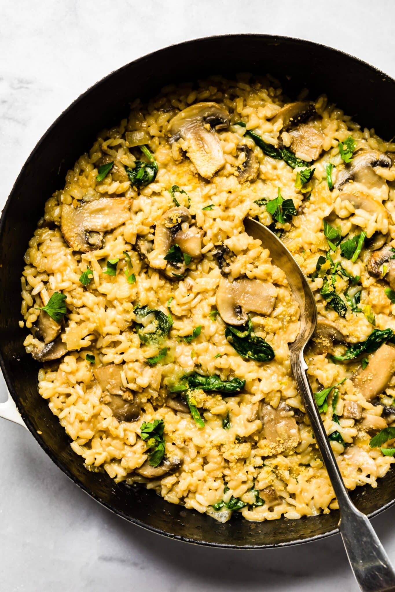 Creamy mushroom risotto in a cast iron pan with spinach and cheese with a spoon.