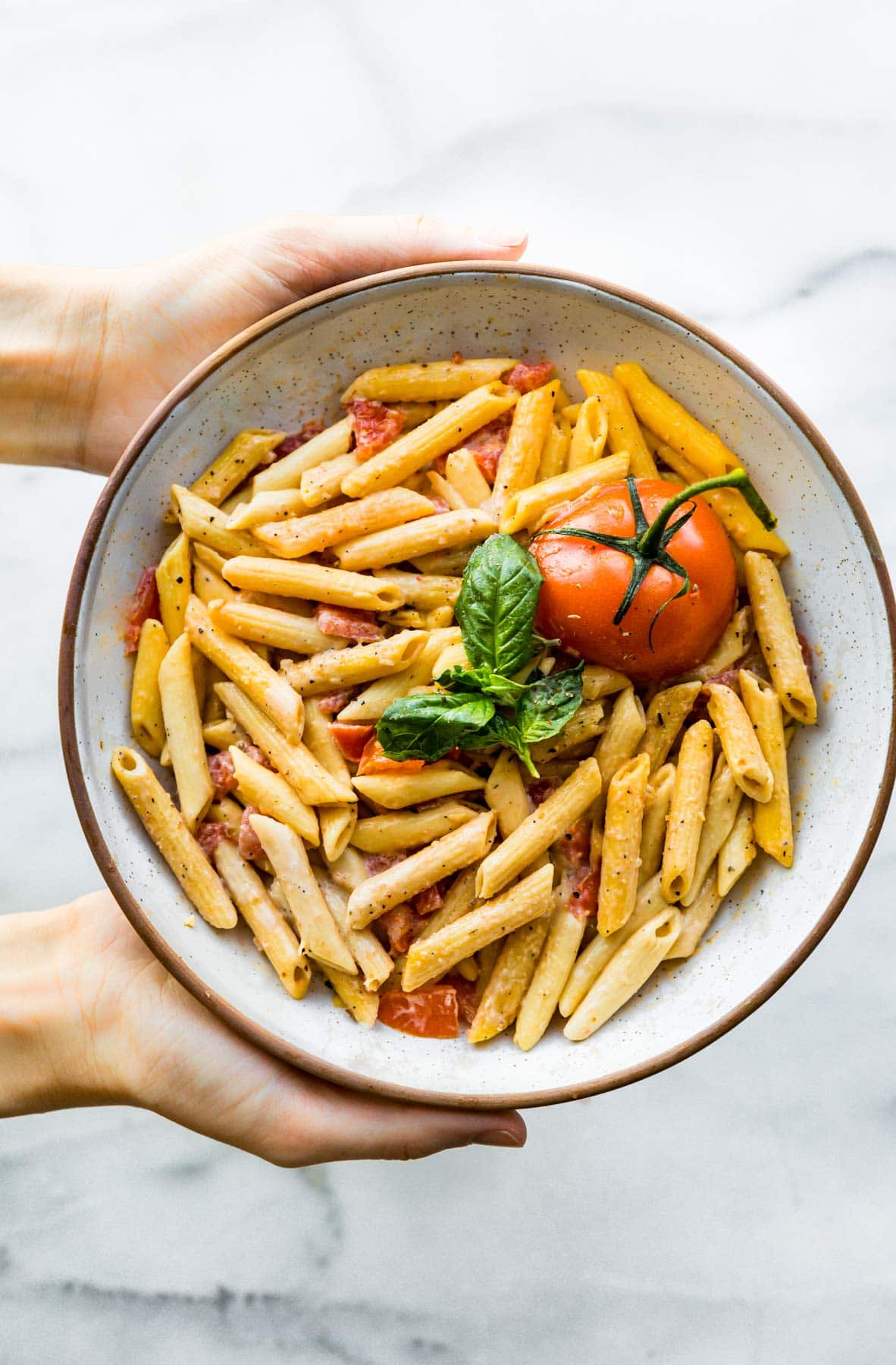 overhead image white bowl of: gluten free pasta (penne pasta) with pieces of fresh tomato and basil