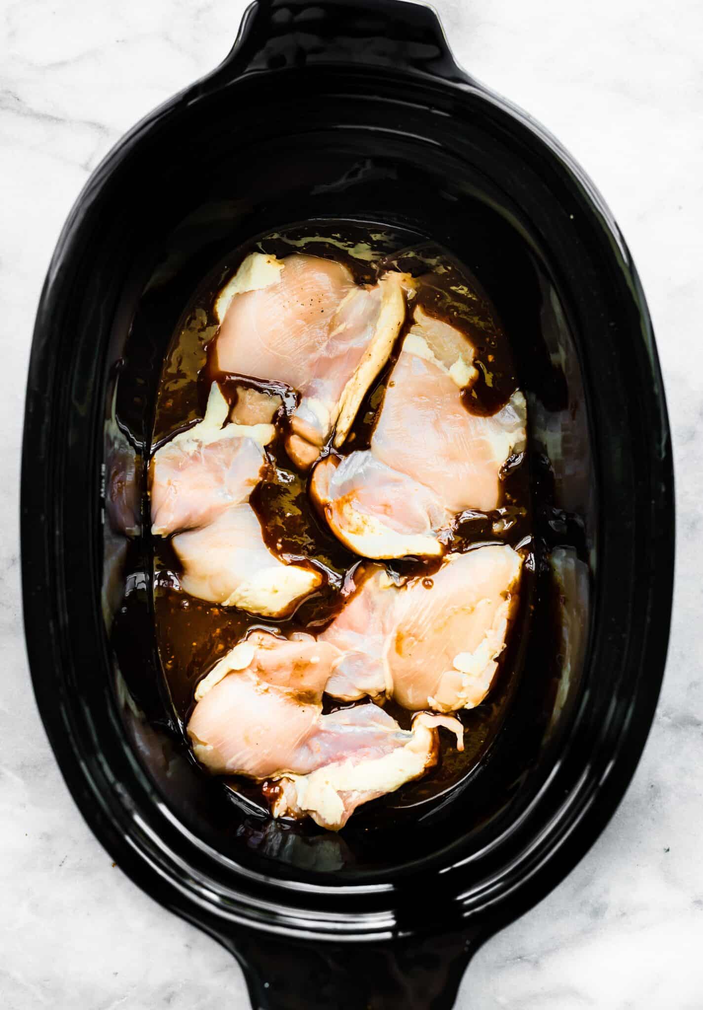 Raw chicken thighs sitting on top of a bbq sauce in a slow cooker.