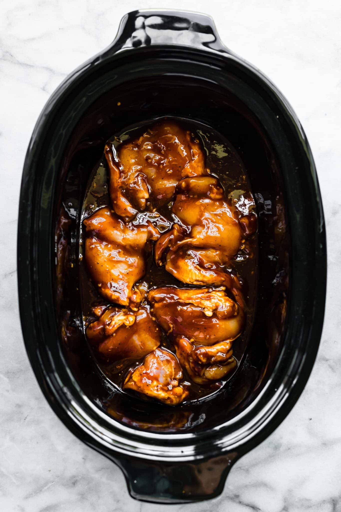 Overhead photo of chicken thighs covered in a bbq sauce in a crockpot.