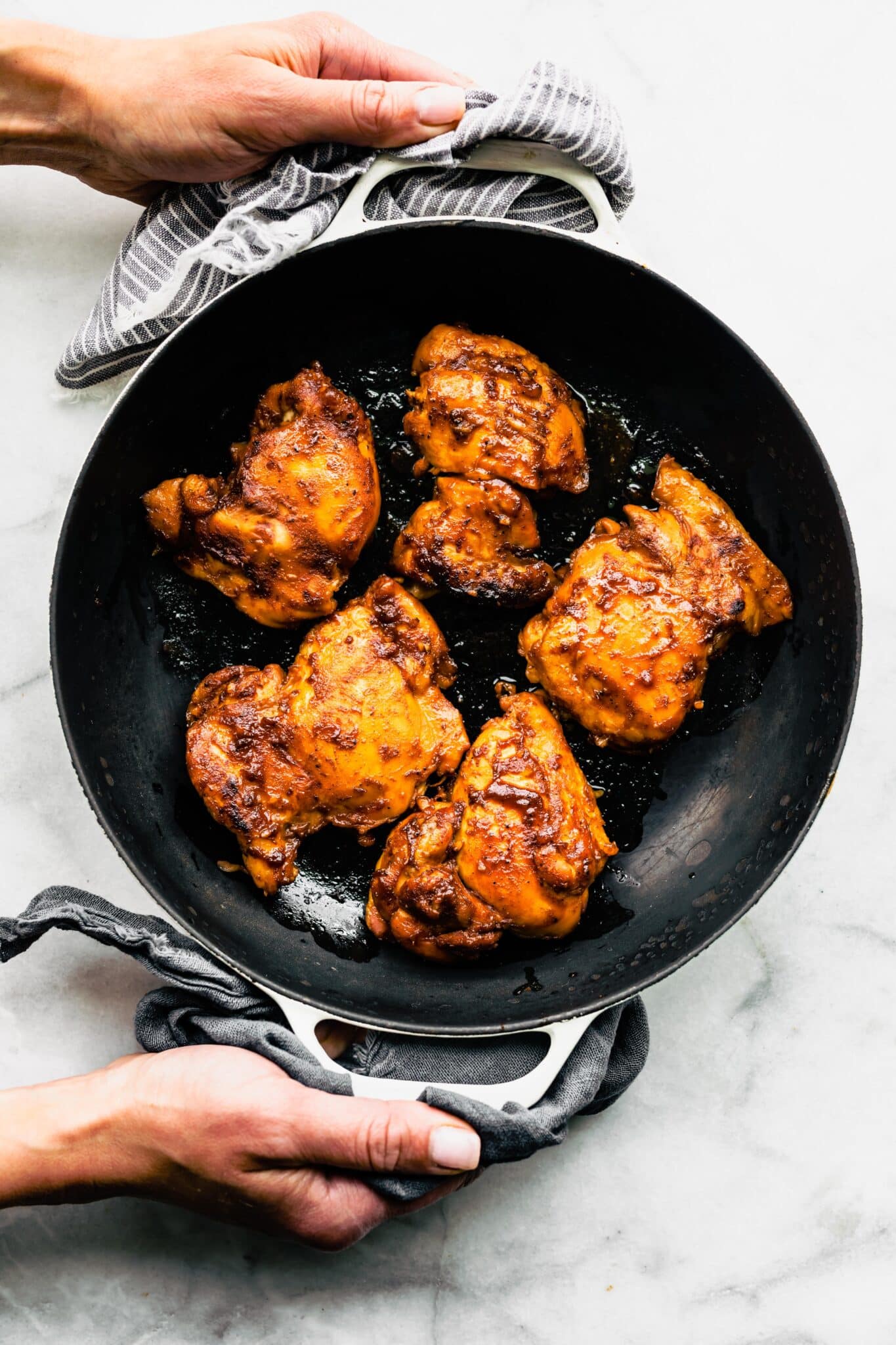 A woman's hands holding a pan with five bbq chicken thighs.