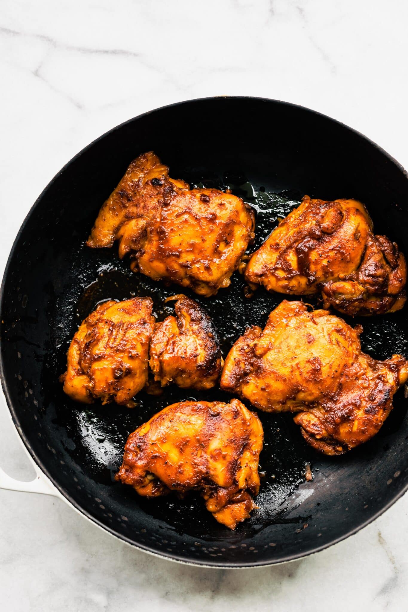 Overhead photo of crockpot bbq chicken thighs in a ceramic skillet.