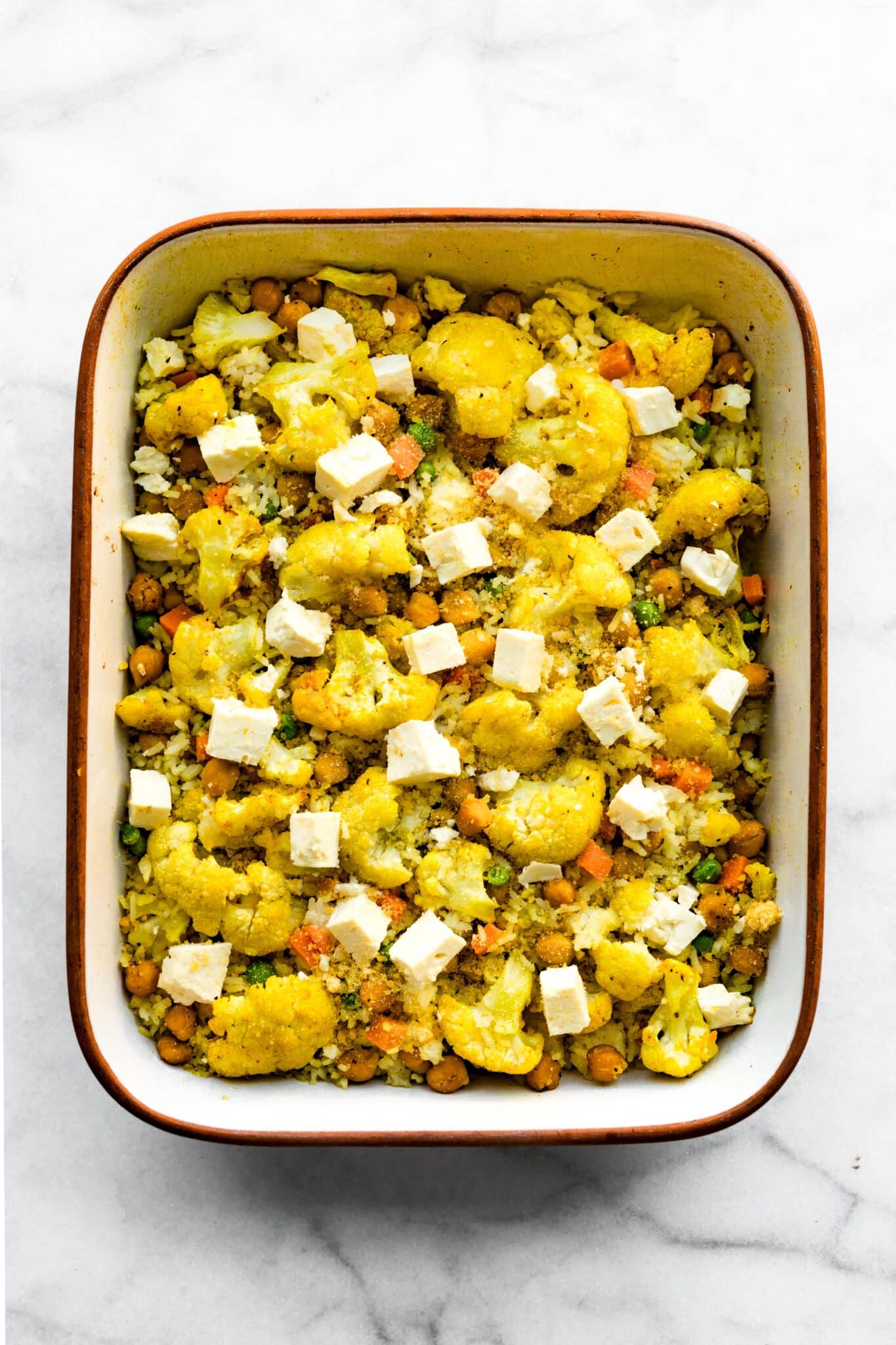 Baked gluten free curried cauliflower with chickpeas in a pan topped with cubed feta cheese.