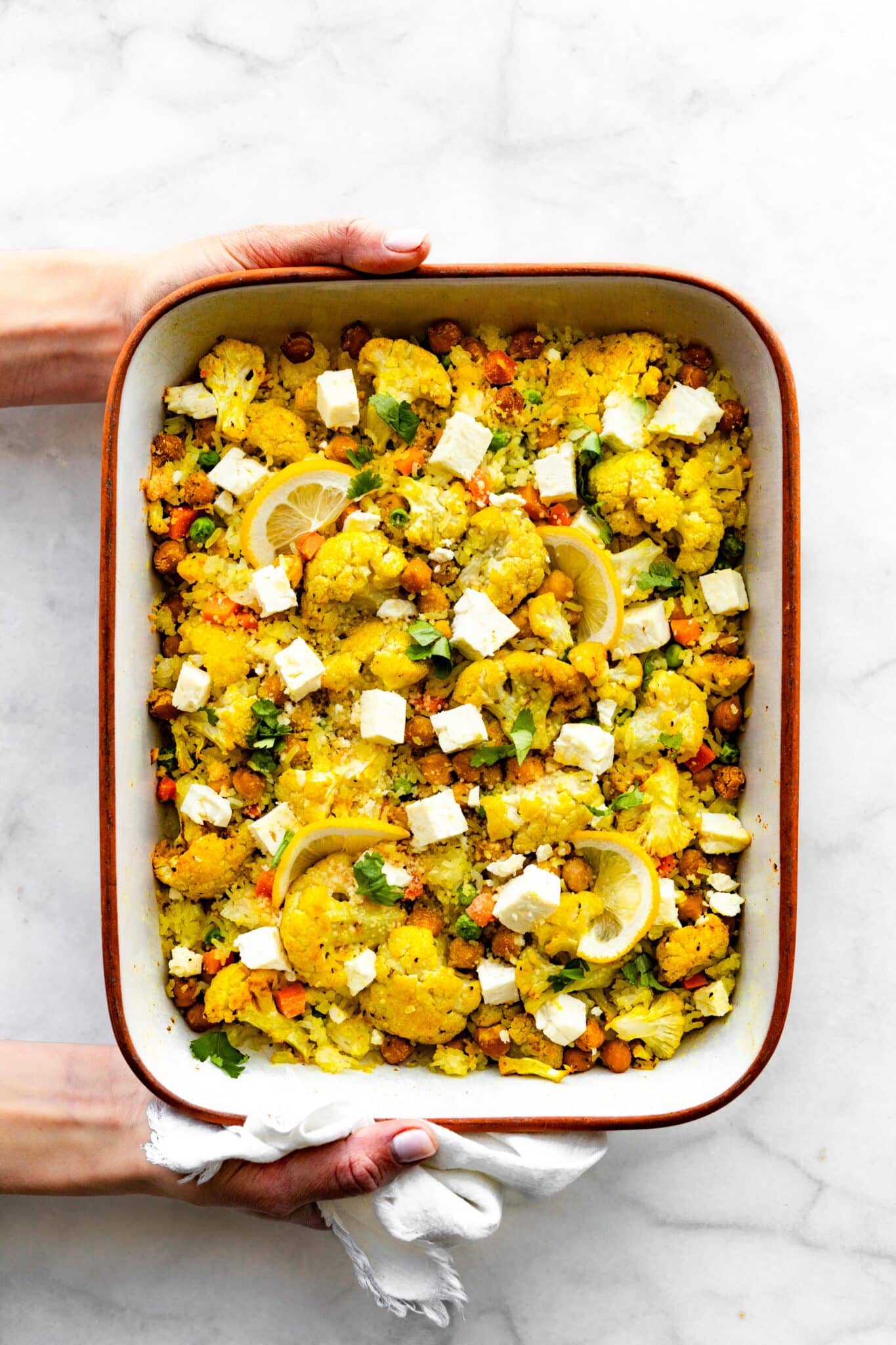 Overhead photo of a woman's hands holding a casserole dish of baked curried cauliflower casserole.